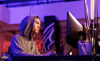 Een jonge gamer in een hoodie achter een pc-opstelling met kleurrijke RGB-verlichting, volledig geconcentreerd op het spel in een moderne gamingomgeving